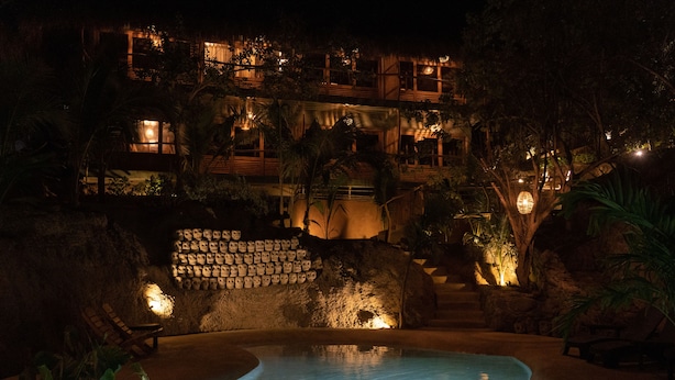 A nighttime view of a resort with a swimming pool, stone walls, and outdoor seating areas. - Cocos Hotel (San Pedro Pochutla)