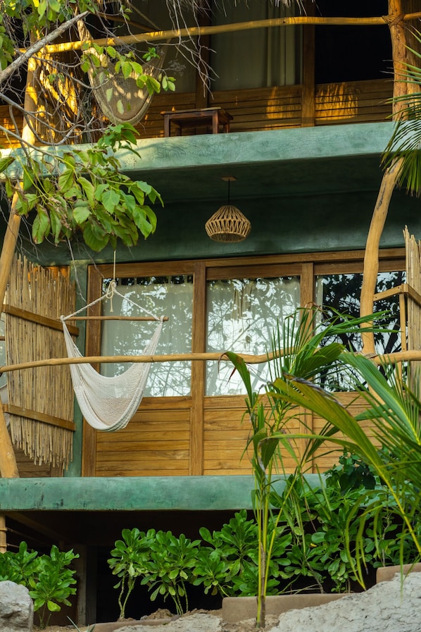 Una cabaña de madera con una hamaca, una lámpara colgante y abundante vegetación.