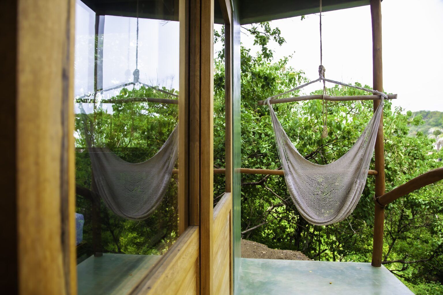 A hammock suspended from a wooden structure, with a view of lush greenery outside.