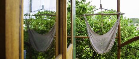 A hammock suspended from a wooden structure, with a view of lush greenery outside.