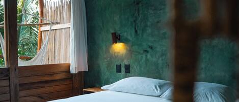 Een kamer met een bed, een hangmat, een raam met gordijnen en een wandlamp.
