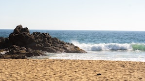 A sandy beach with a rocky outcrop and waves crashing onto the shore. - Cocos Hotel (San Pedro Pochutla)
