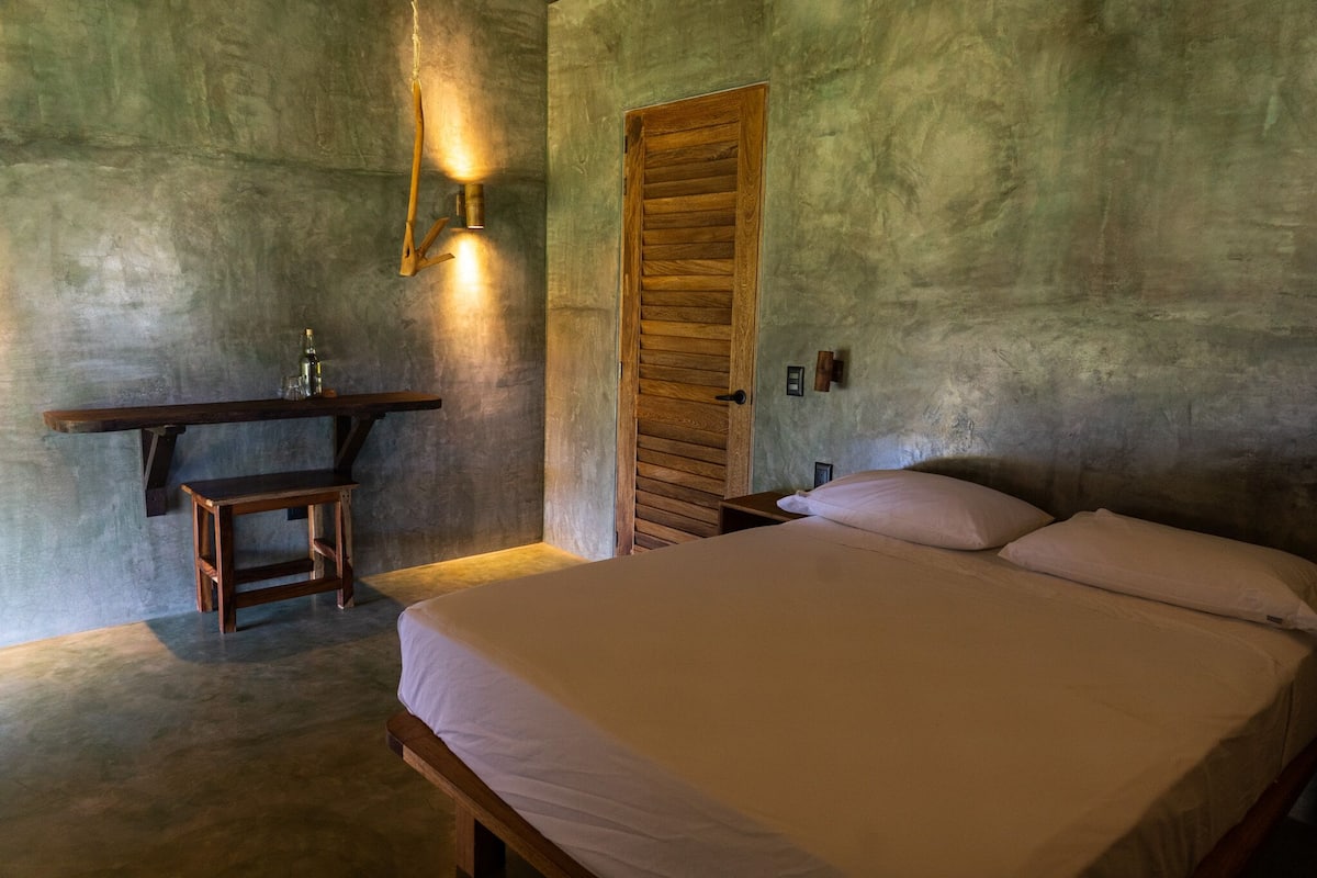 Ein Schlafzimmer mit einem Bett, einem Nachttisch, einer Holzbank und einer Wandleuchte.