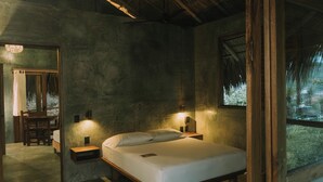 A bedroom with a wooden bed, nightstands, a mirror, and a window with a view of greenery. - Cocos Hotel (San Pedro Pochutla)