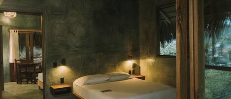 A bedroom with a wooden bed, nightstands, a mirror, and a window with a view of greenery.