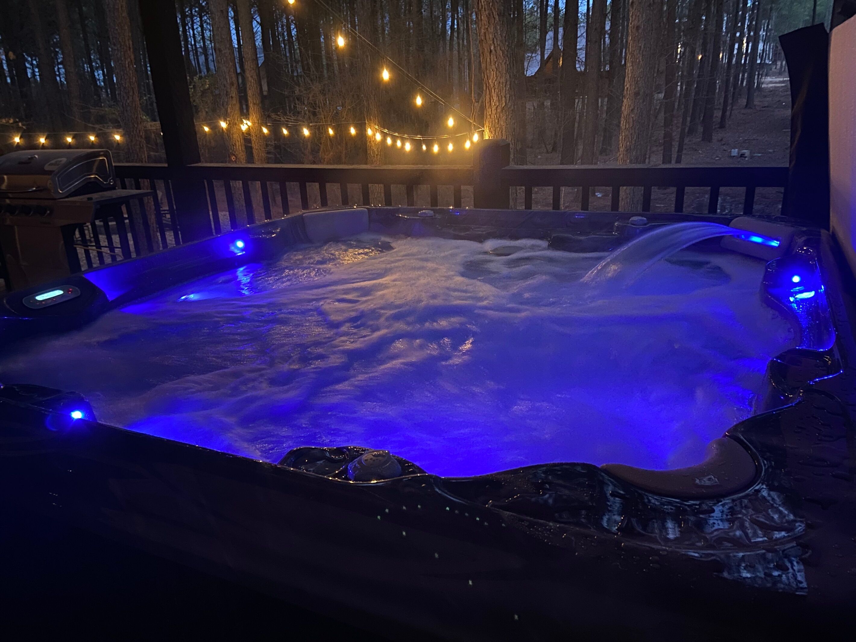 A hot tub with blue lighting, surrounded by a wooden deck and string lights.