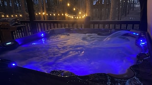 Un bain à remous doté d’un éclairage bleu, entouré d’une terrasse en bois et illuminé de guirlandes lumineuses.