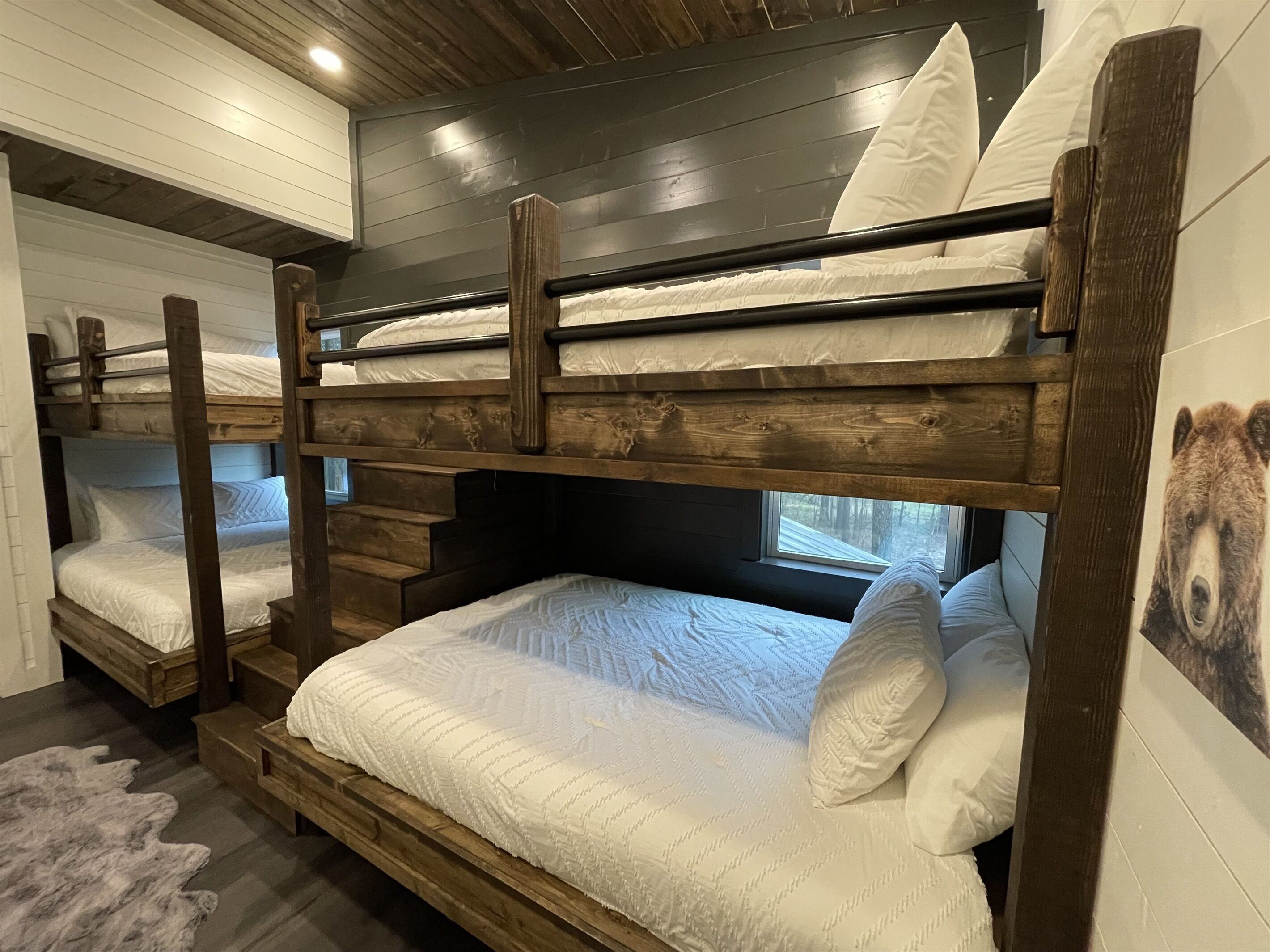 Dormitorio con literas, cabeceros de madera, ropa de cama blanca y un cuadro de un oso en la pared.