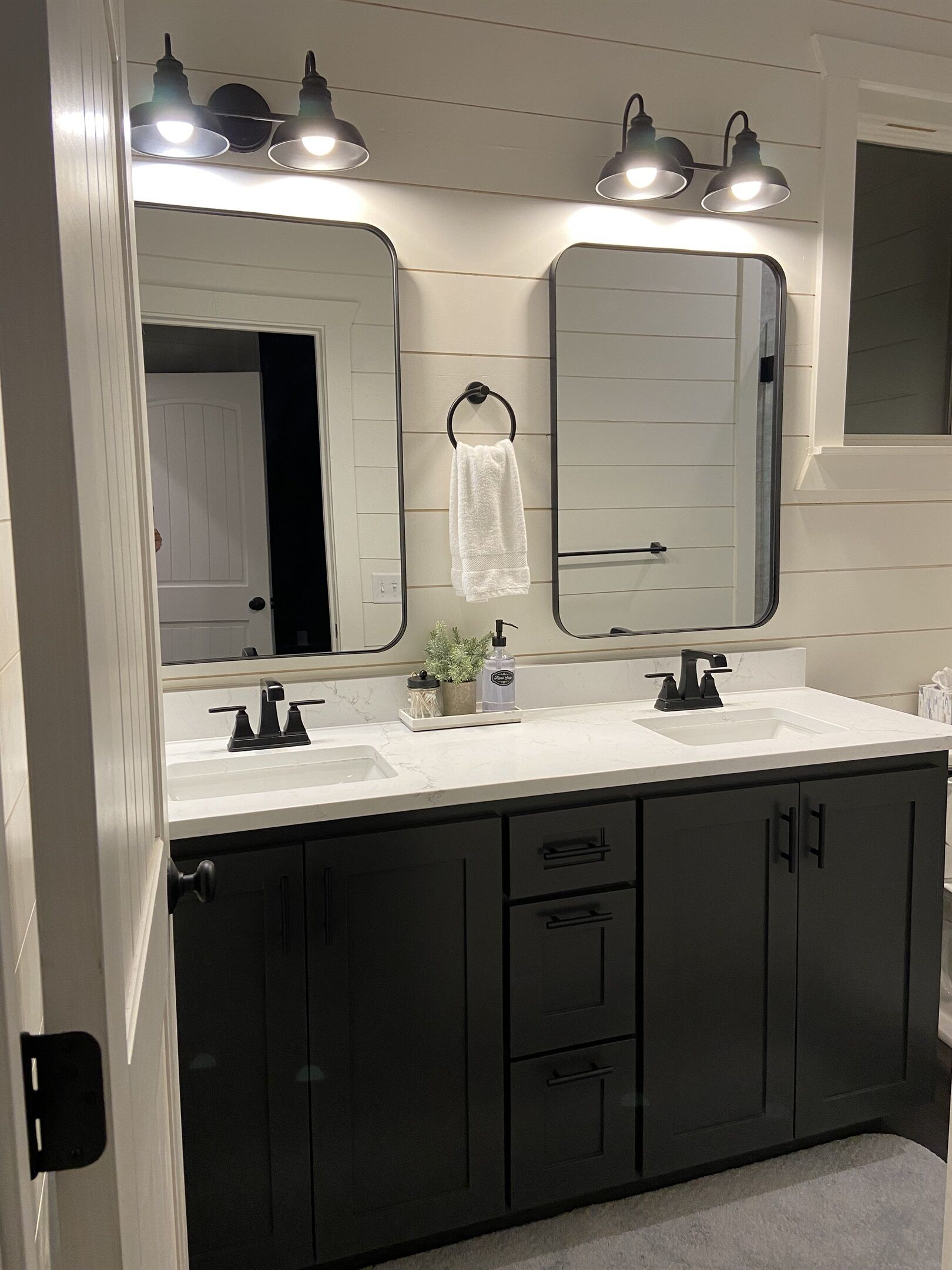 A bathroom with two sinks, dark cabinets, a towel hanging on a ring, and three wall-mounted lights.