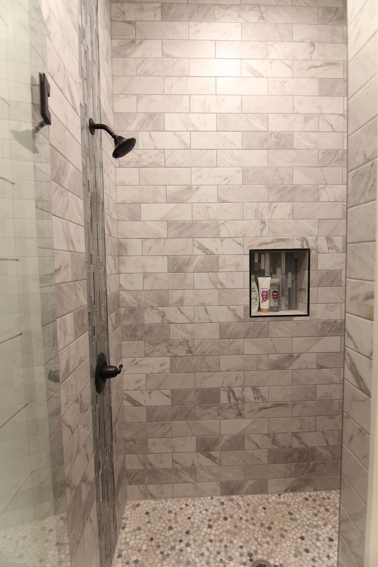Une douche avec un mur carrelé, une petite étagère contenant des articles de toilette et un sol décoré de motifs de galets.