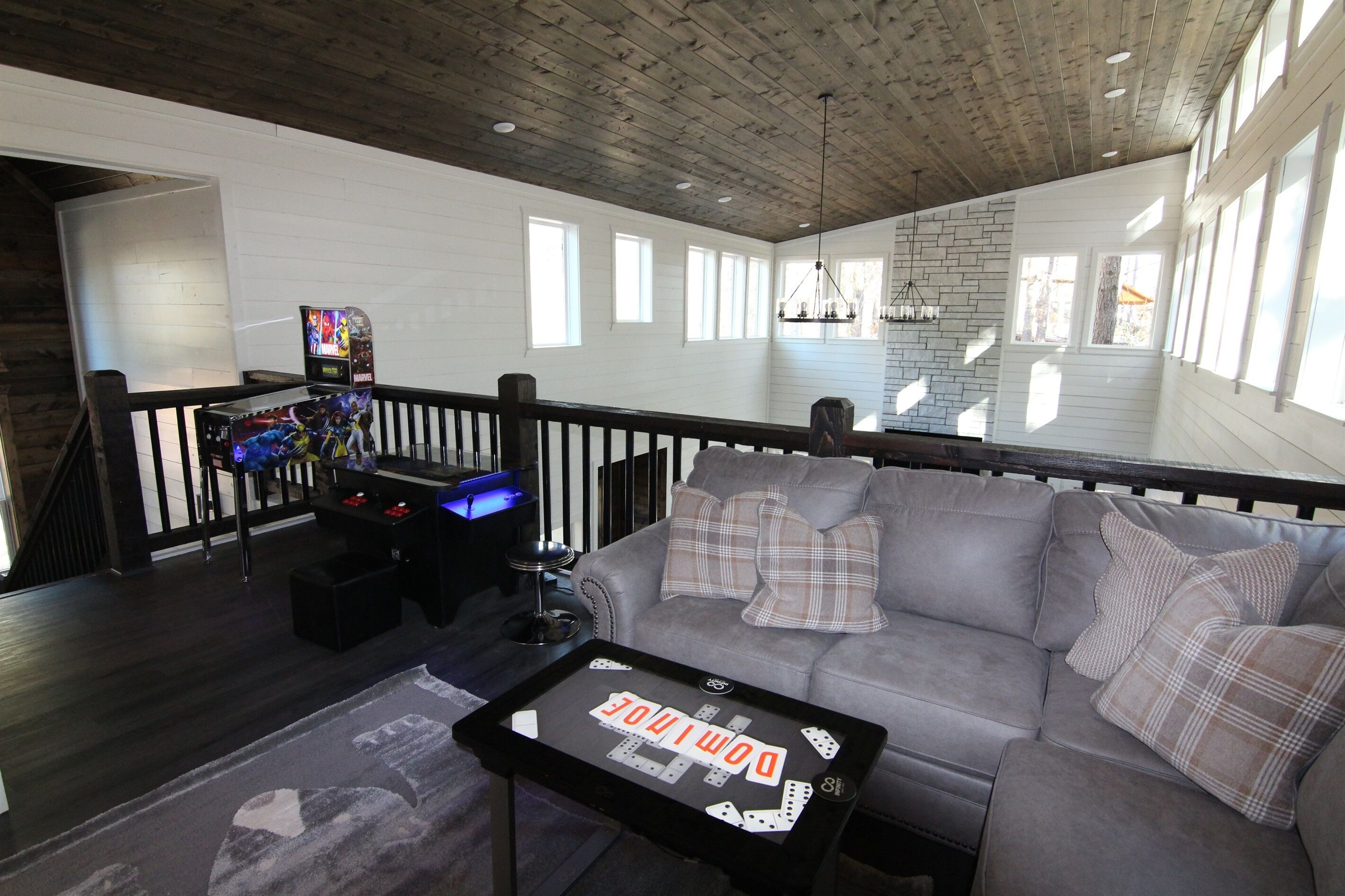 A spacious living area with a grey sofa, a coffee table with dominoes, and a gaming console.