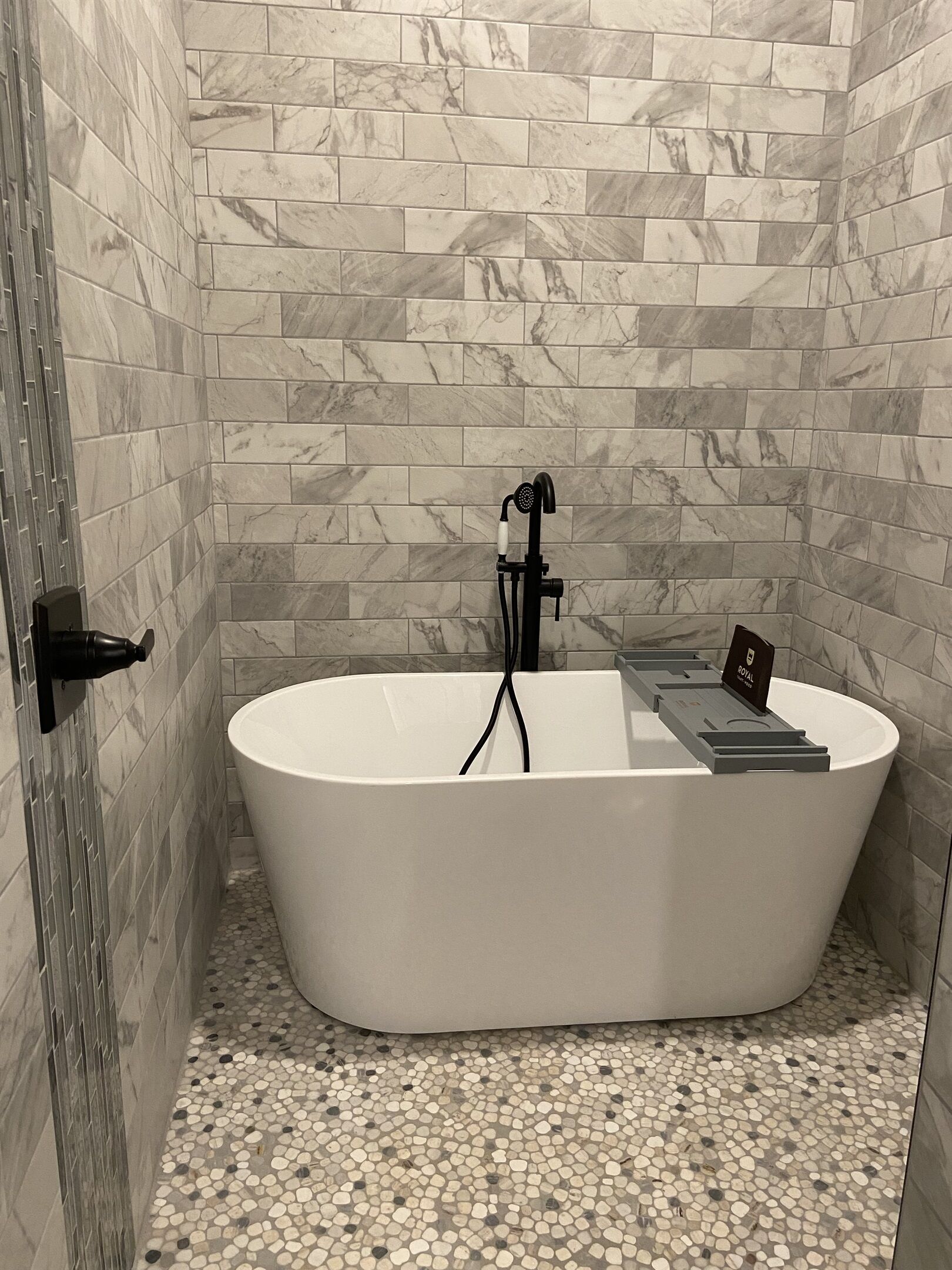 A modern bathroom with a freestanding bathtub, marble wall tiles, and a pebble-patterned floor.