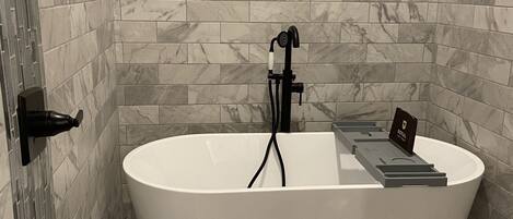 A modern bathroom with a freestanding bathtub, marble wall tiles, and a pebble-patterned floor.