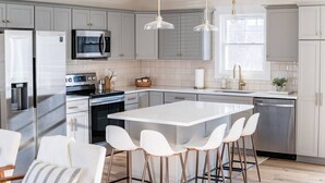 A modern kitchen with grey cabinets, stainless steel appliances, a central island with bar stools, and pendant lighting.