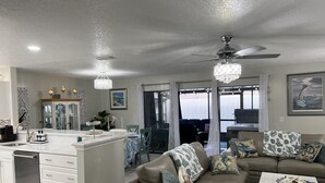 A modern kitchen with white cabinetry, a central island, and a dining area with a sofa and coffee table.