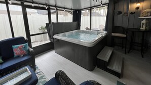 A covered outdoor area with a hot tub, seating, and a bar area.