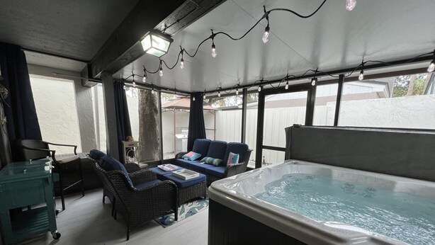 A covered outdoor area with a hot tub, wicker furniture, and string lights.