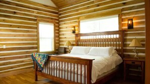 A log cabin bedroom with a wooden bed, two bedside lamps, and a window. - Minutes from Baum Stadium with a View! (Fayetteville)