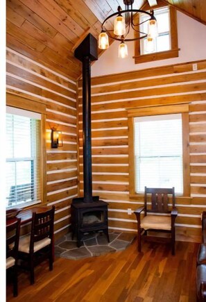 A log cabin interior with a central fireplace, wooden walls, and a stone hearth.