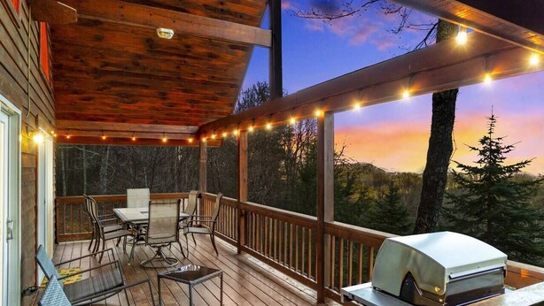 A wooden deck with outdoor furniture and a grill, overlooking a forested area.