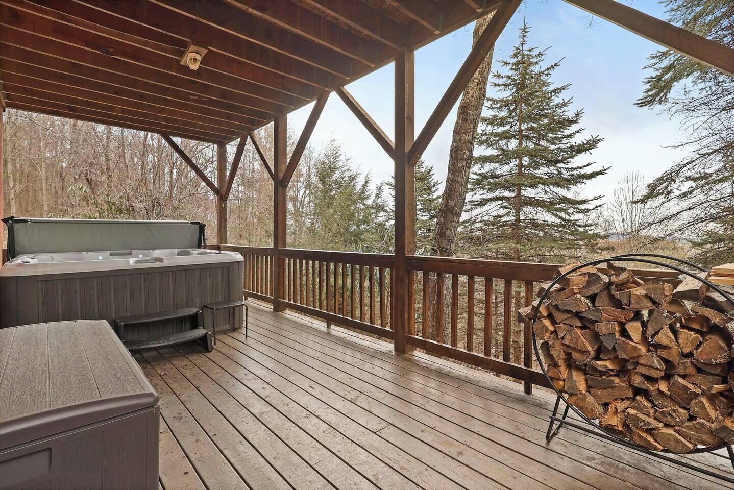 A wooden deck with a hot tub, a grill, and a stack of firewood.