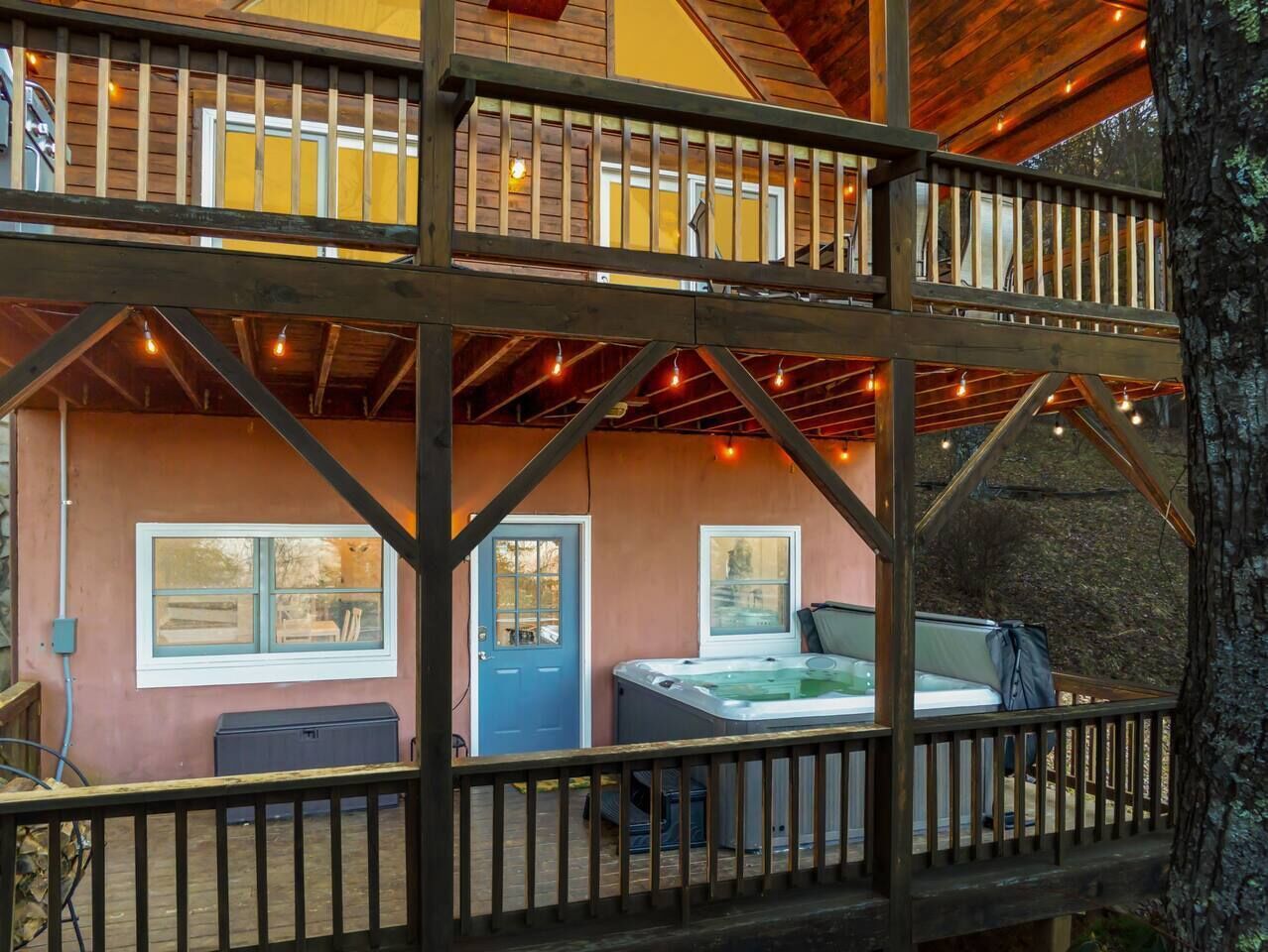 Une cabane à deux étages dotée d’un jacuzzi au deuxième étage, d’une terrasse avec une balustrade et offrant une vue sur le paysage environnant.