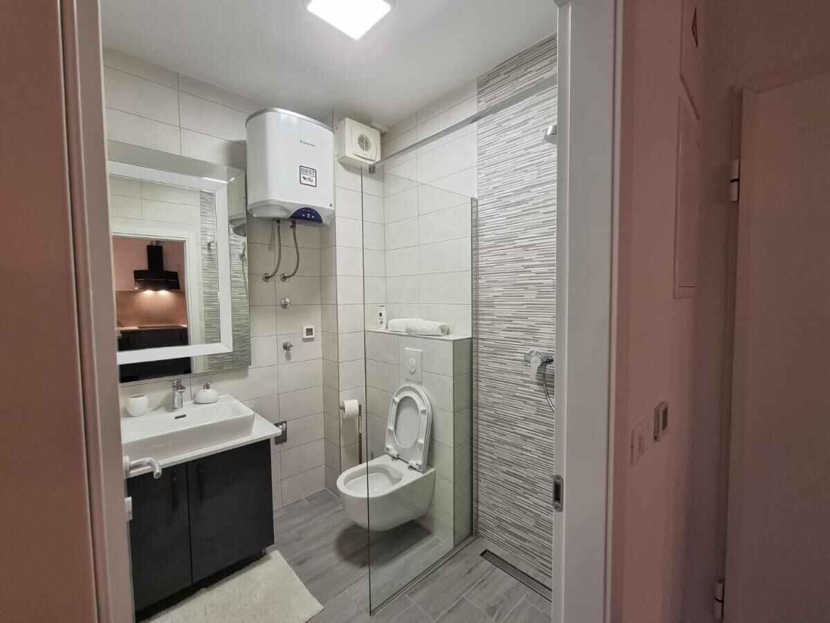 Une salle de bain moderne avec une douche à parois de verre, des toilettes blanches et un lavabo avec un miroir au-dessus.