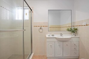 A bathroom with a glass shower enclosure, a sink with a mirror above, and a potted plant on the counter.