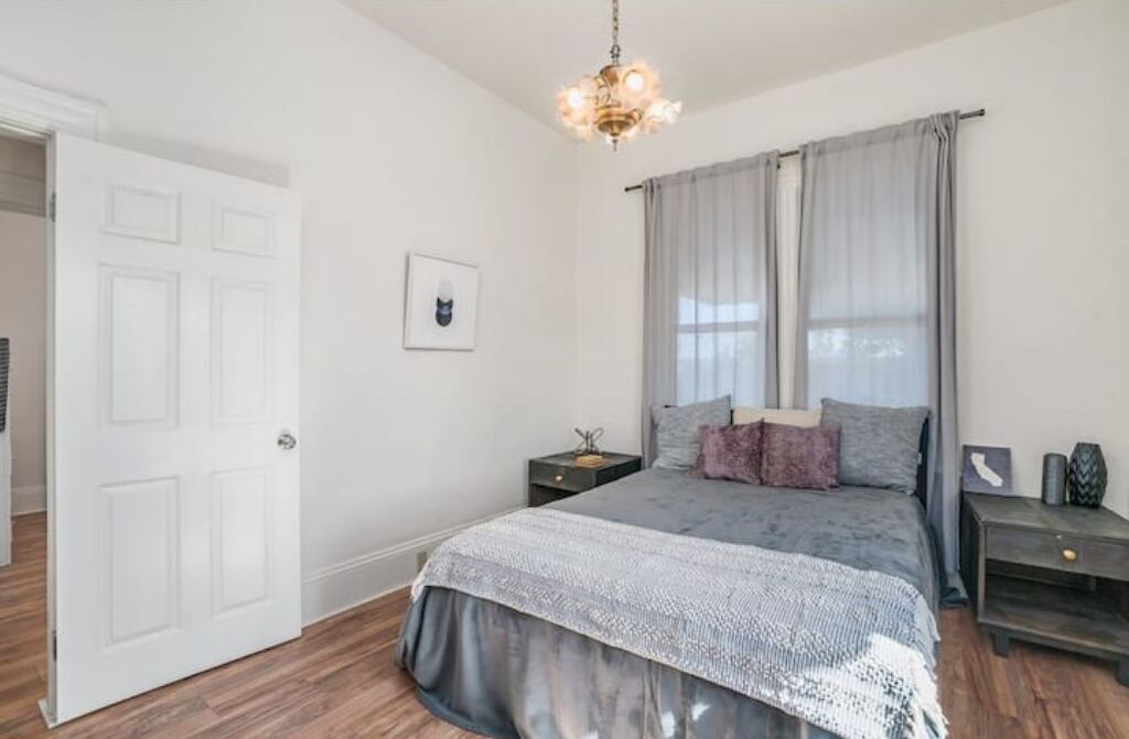 A bedroom with a bed, a nightstand, a chandelier, and a door.