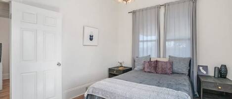 A bedroom with a bed, a nightstand, a chandelier, and a door.