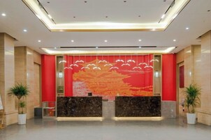 Zona de recepción con fondo rojo, mostrador de mármol y plantas en macetas.
