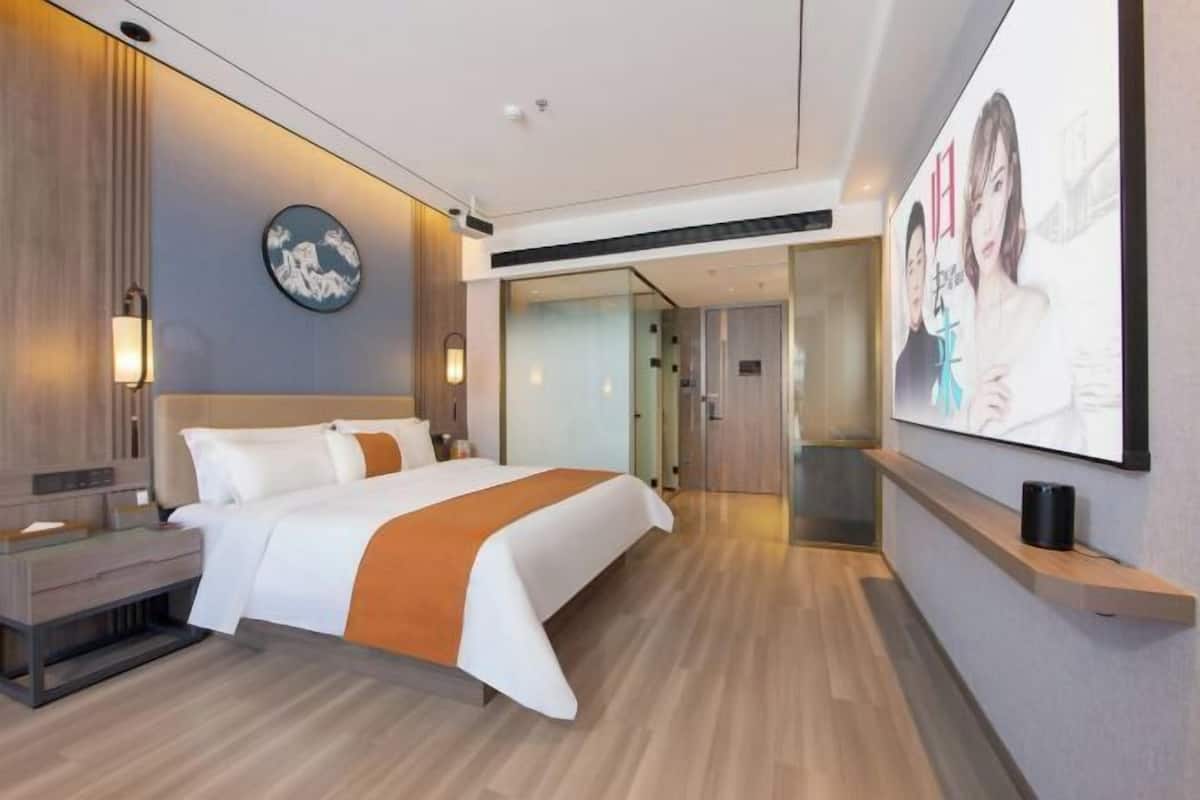 Et moderne hotelværelse med en stor seng, sengeborde, et vægmonteret TV og trægulv.