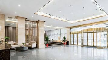 Eine geräumige Lobby im modernen Stil, mit einer Rezeption, einer Sitzecke und einer Treppe zu einer oberen Ebene.