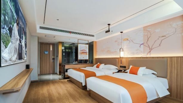 A hotel room with two beds, wooden flooring, a large mirror, and artwork on the walls. - Dongtingchun (Shuangfeng)