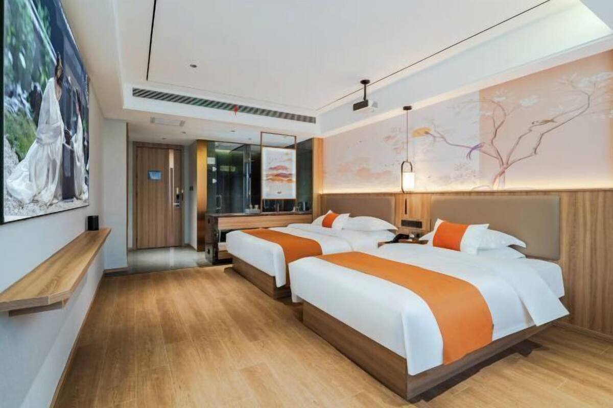 A hotel room with two beds, wooden flooring, a large mirror, and artwork on the walls.