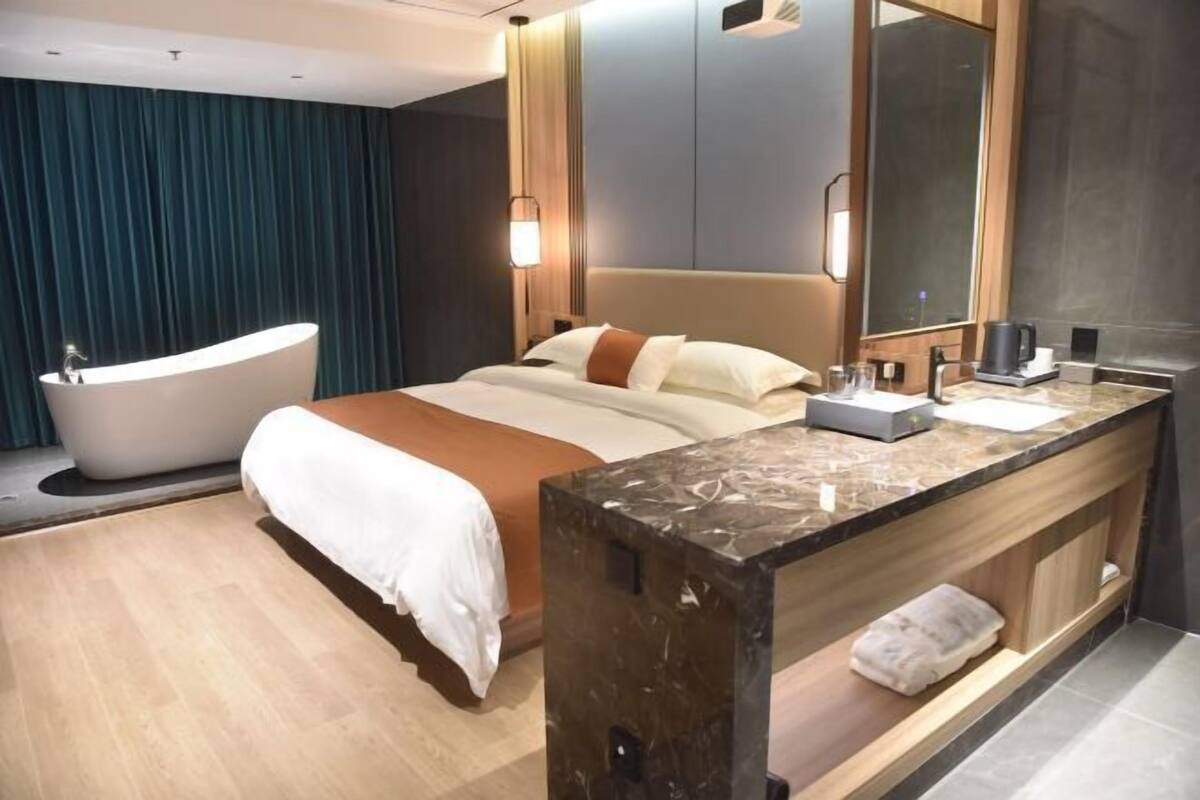 A modern hotel room with a large bed, a separate bathroom with a freestanding bathtub, a marble vanity, and a large mirror.