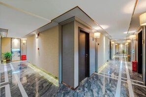 A hotel corridor with a marble floor, a door, and a red trash bin.