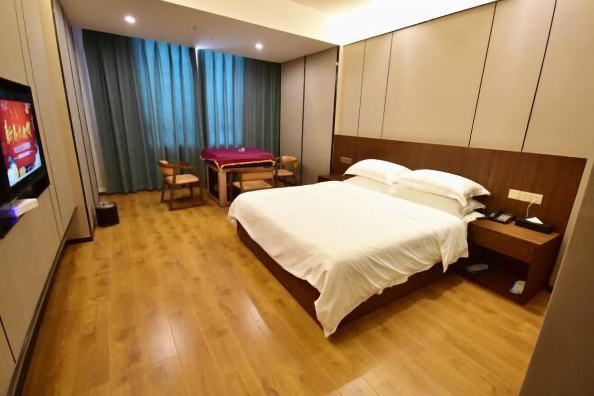 A hotel room with a bed, bedside table, TV, and a small desk with a chair.