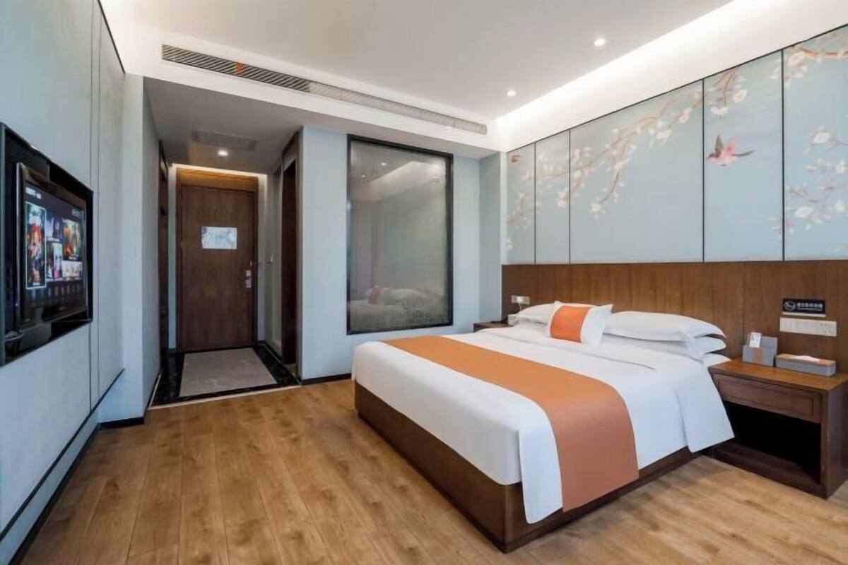A hotel room with a large bed, a wooden headboard, a wall-mounted TV, and a sliding door leading to a bathroom.