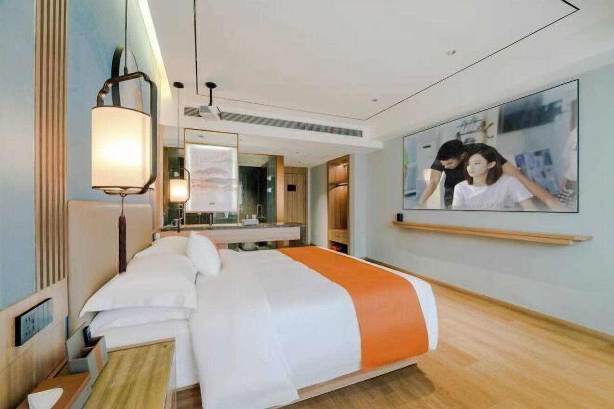 A hotel room with a bed, a large mirror, a wall-mounted TV, and a wooden floor.