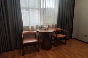 A room with a round wooden table, two leather chairs, a window with sheer curtains, and a bottle of water on the table.