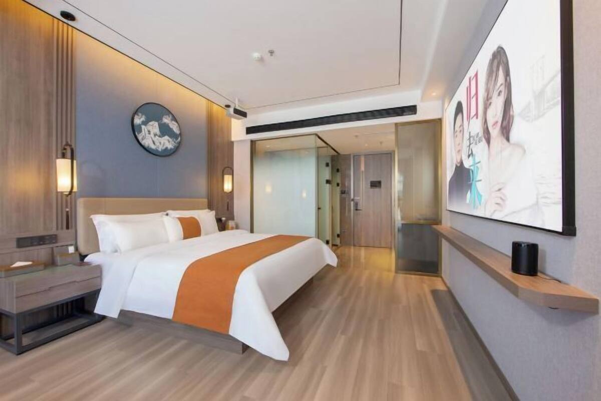 A modern hotel room with a large bed, bedside tables, a wall-mounted TV, and a wooden floor.
