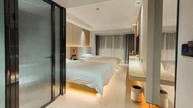A modern hotel room with a large bed, a separate seating area, a mirror, and a small trash bin. - Alant Hotel (Duyun)