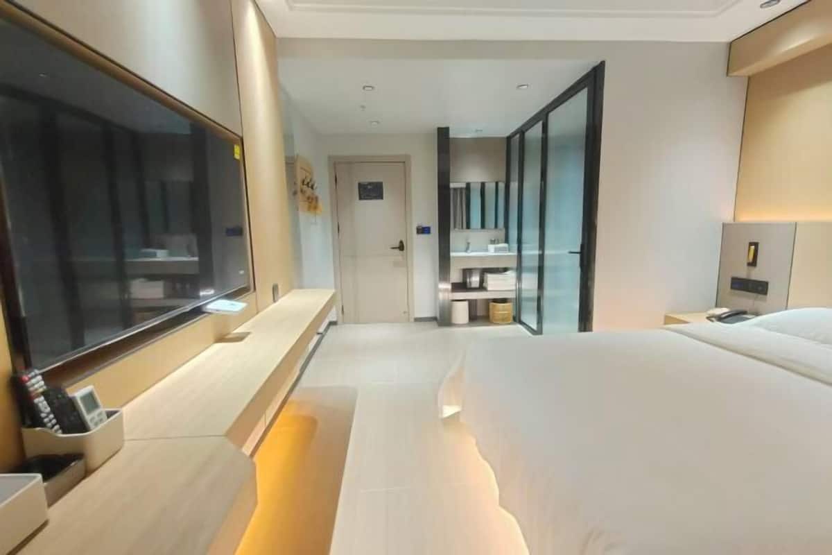 Une chambre d’hôtel moderne dotée d’un grand lit, d’une télévision, d’un bureau avec un téléphone et d’une salle de bain avec un miroir et un lavabo.