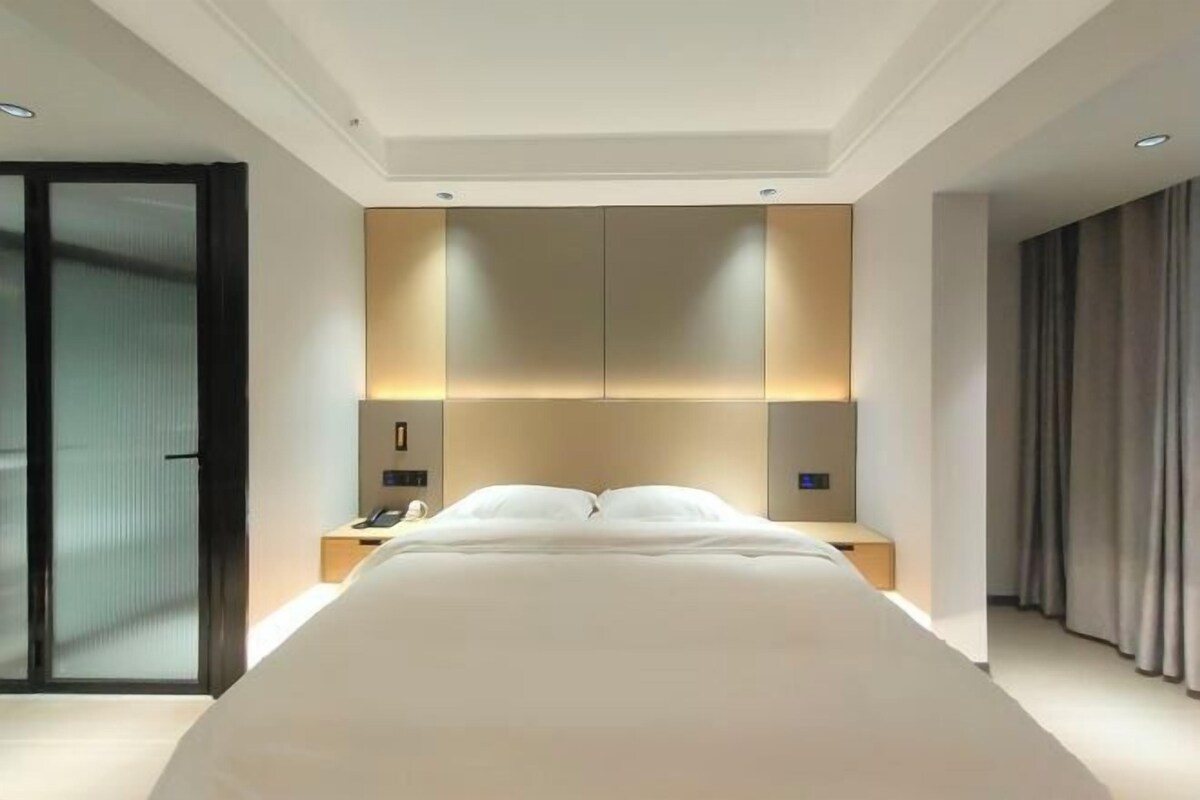 A modern hotel room with a large bed, a bedside table, a nightstand, and a wall-mounted light fixture.