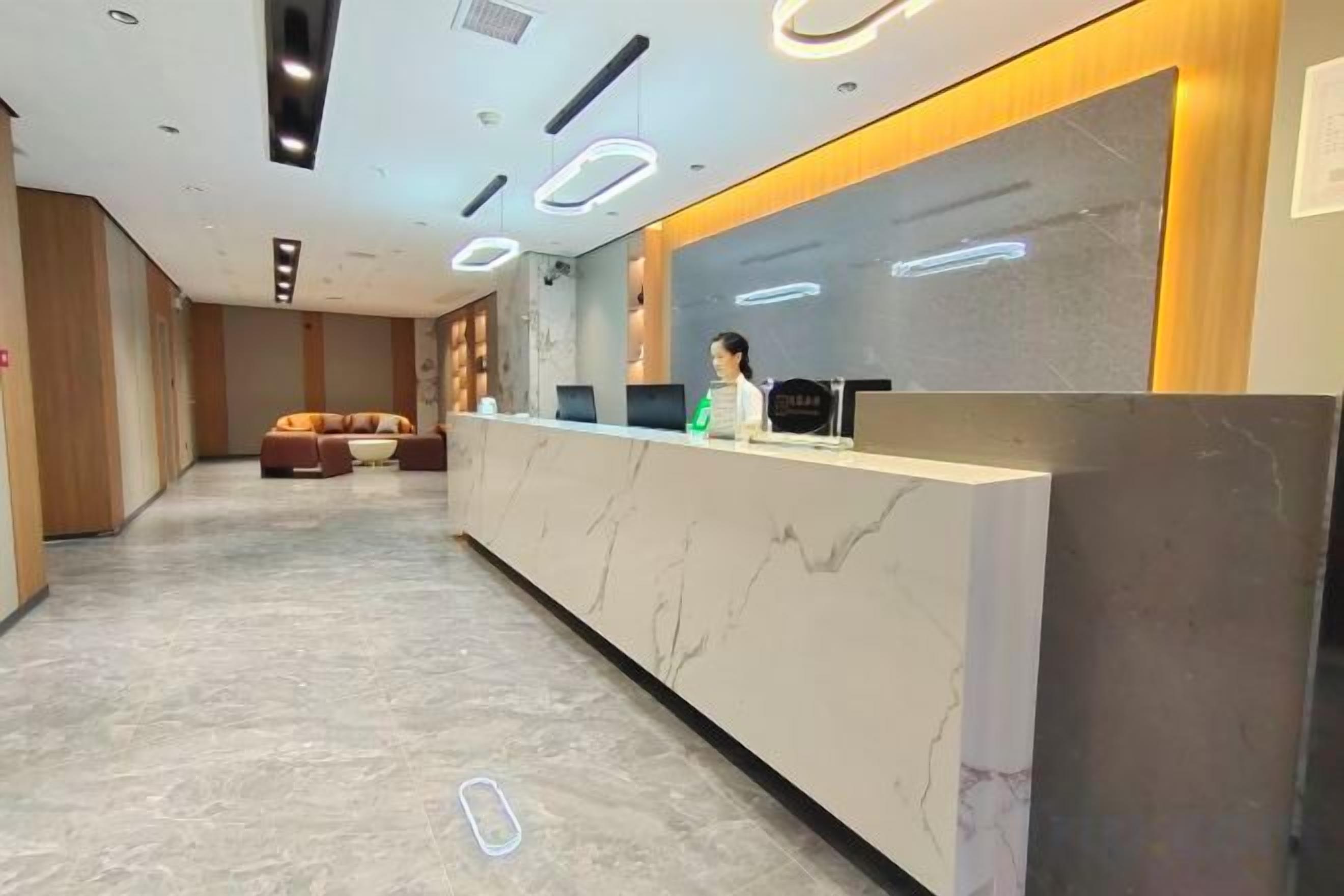 A hotel reception area with a marble reception desk, a sofa, and a counter with a person behind it.