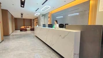 A hotel reception area with a marble reception desk, a sofa, and a counter with a person behind it.