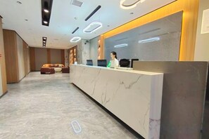 A hotel reception area with a marble reception desk, a sofa, and a counter with a person behind it. - Alant Hotel (Duyun)