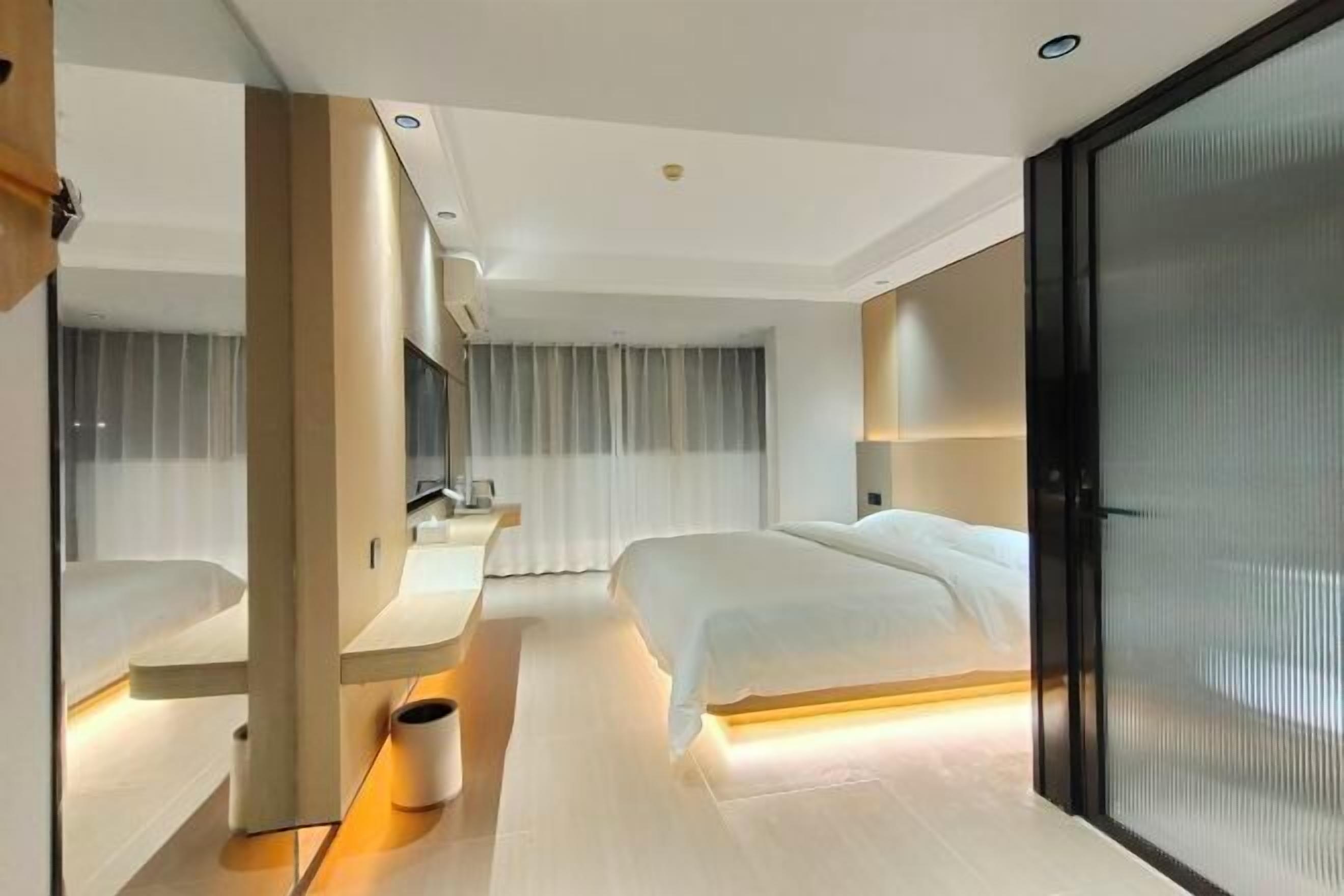 Een moderne hotelkamer met een groot bed, een bureau en een glazen scheidingswand.