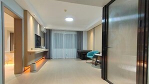 A modern hotel room with a large sliding door, a flat-screen TV mounted on the wall, a small table with a chair, and a large window with curtains. - Alant Hotel (Duyun)